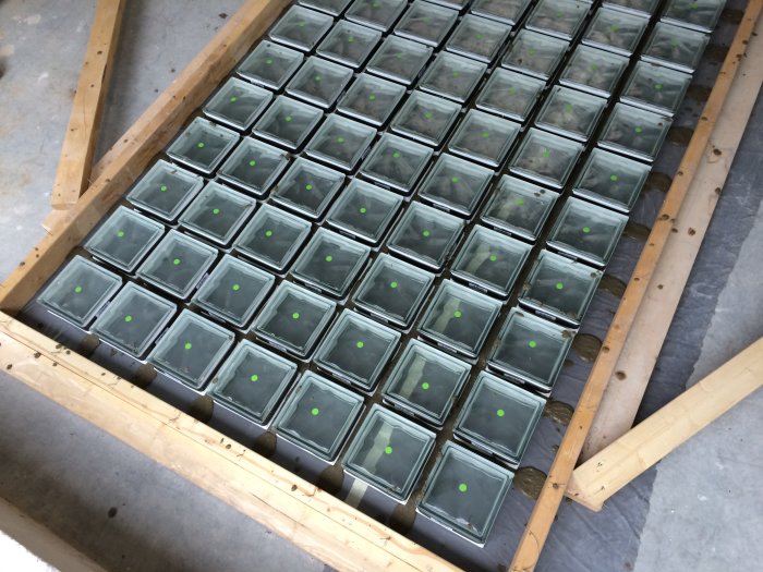 Glasblock ordnade i rader inom en träform på golvet, förberedda för gjutning till ett fönsterparti.