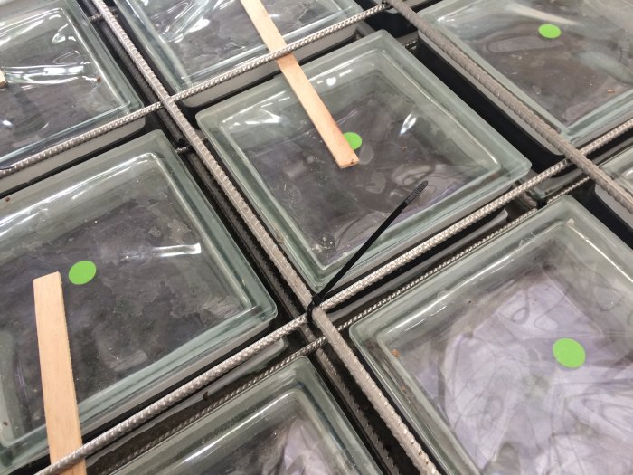 Glasblock monterade i en form med armeringsjärn och grön markering, förberedda för gjutning till ett stort fönster.