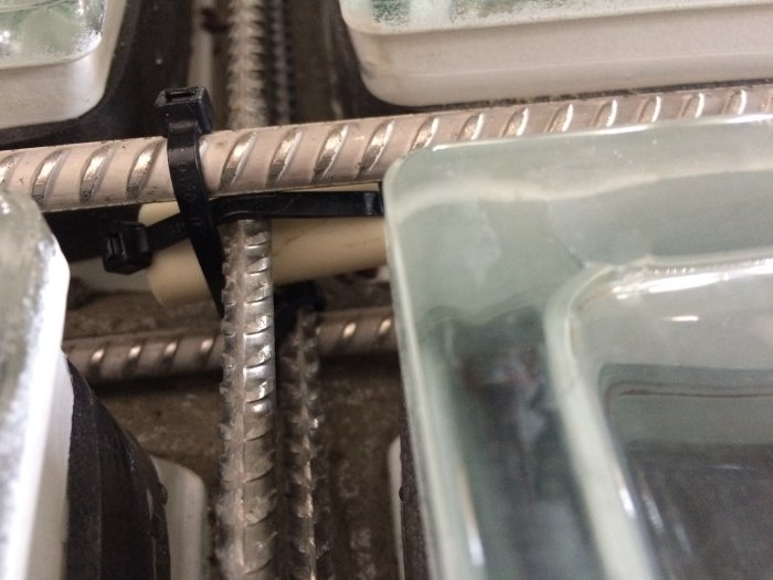 Armeringsjärn fixerade med plastbuntband nära kanten av ett glasblock under byggprocessen.