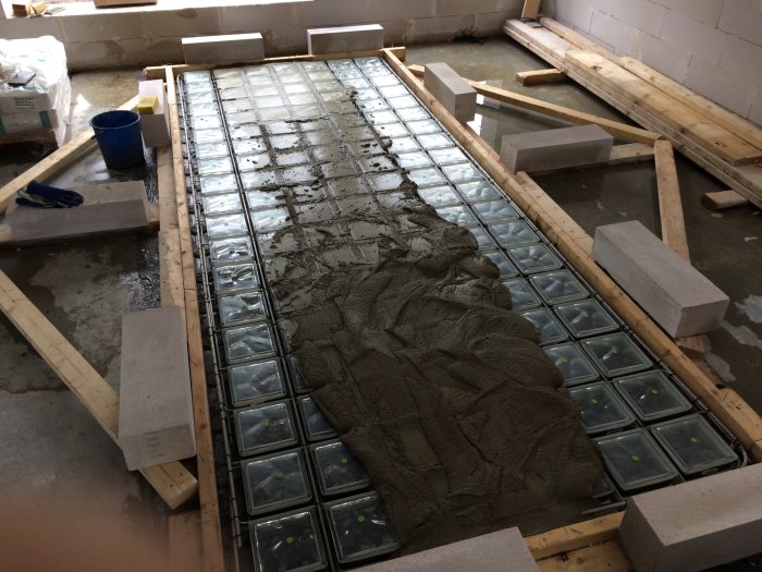 Gjutning av betong över glasblock i en konstruktionsprocess, med verktyg och byggmaterial synliga.