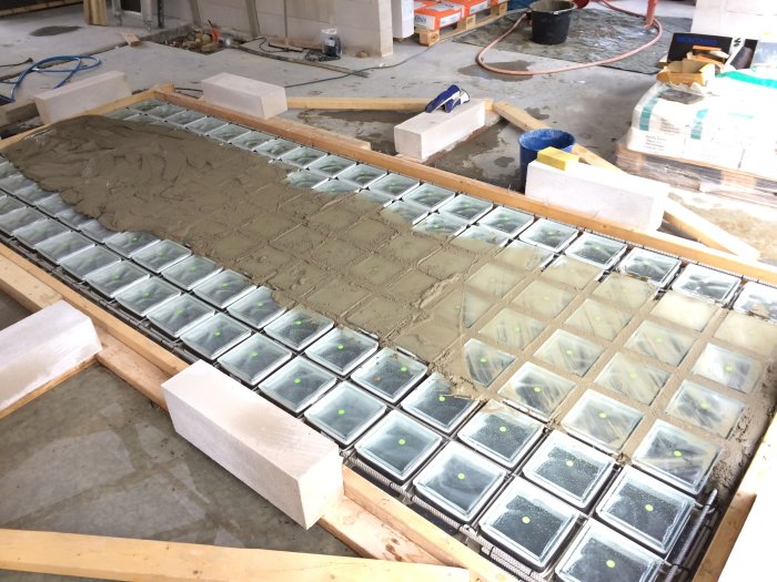 Gjutning av betong över glasblock i en byggnation, med delvis gjutna ytor och förberedande material runtomkring.