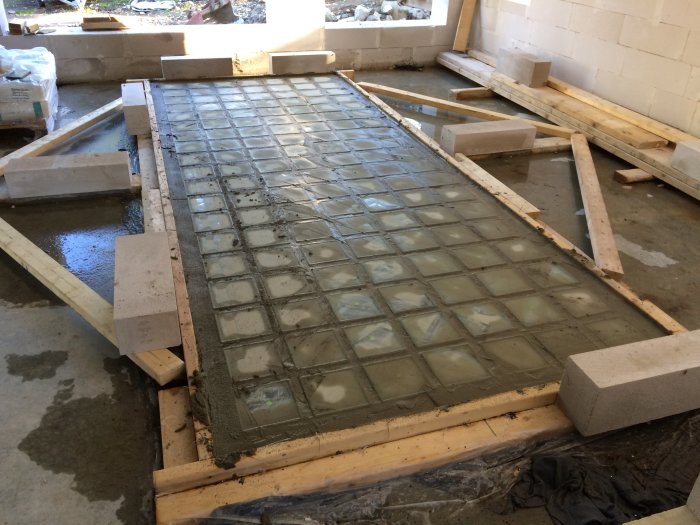 Gjutning av betong över glasblock inramat av träformar och stödblock i en byggmiljö.