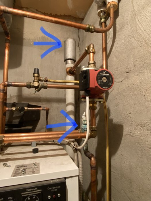 Värmesystem med kopparledningar, cirkulationspump och avstängningsventiler markerade med blå pilar.
