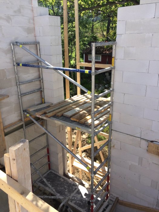 Ställning uppbyggd i öppning för glasblocksfönster under installation i en vit murad vägg på byggplats.