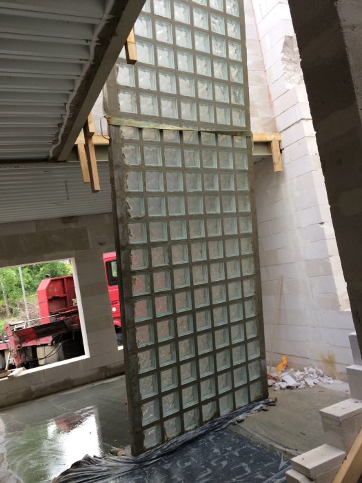 Stort glasblocksfönster som lyfts upp på en byggplats, omgivet av Lättklinkerblock och byggmaterial.