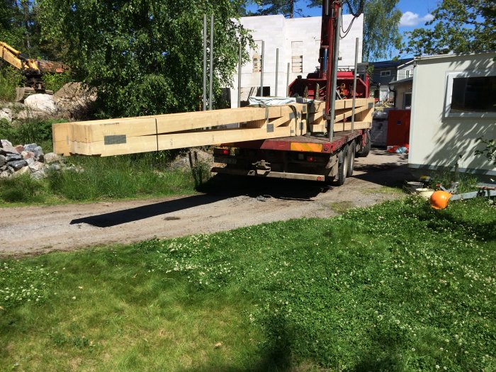 Lastbil levererar stora trälådor med takstolar på en byggarbetsplats.