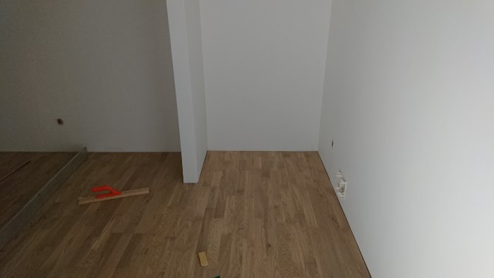 Nyinstallerat trägolv med en handsåg och rester av byggmaterial på golvet i ett tomt rum.