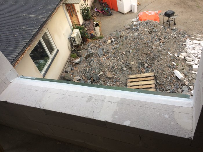 Galvad plåt och tätskikt på fönstersmyg vid byggprojekt, med utsikt över en byggplats.