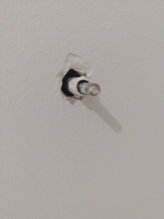 Hål i vitmålad lättbetongvägg med ett lossnat metalliskt radiatorfäste och synliga skador runtom.