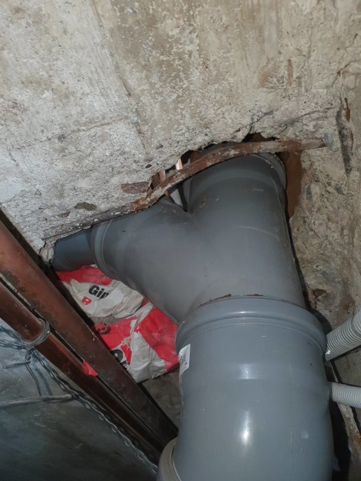 Rörledning som passerar genom ett hål i ett betongbjälklag med synliga sprickor och otätade utrymmen.