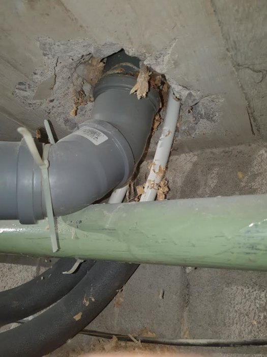 Hål i betong med rör och kablar genomföring, otätat med synligt grus och isoleringsmaterial runtomkring.