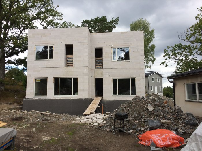 Nybyggt hus med nyligen monterade stora fönster, byggmaterial och röran på marken.
