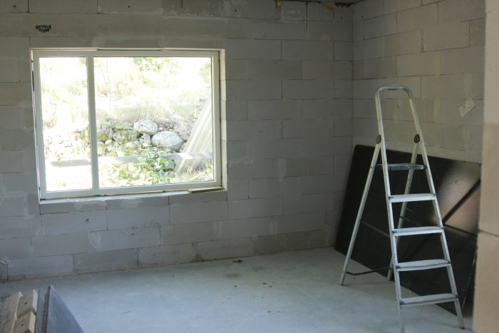 Nyinstallerat mindre fönster i en grå betongvägg i ett rum under renovering med en stege till vänster.
