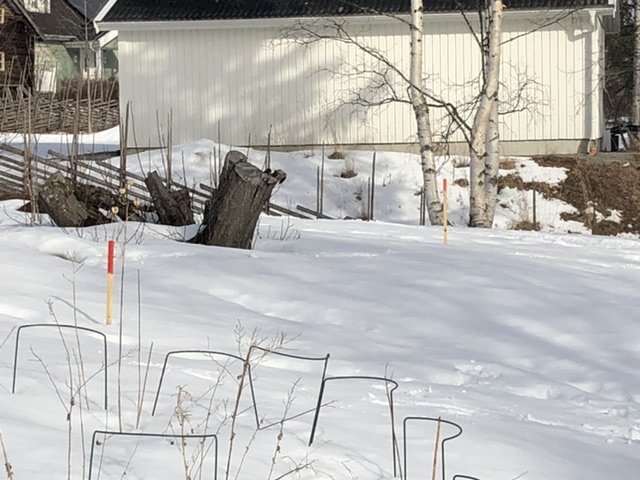 Snötäckt tomt markerad med rödgul markör där ett nytt garage ska byggas, intill befintligt hus.