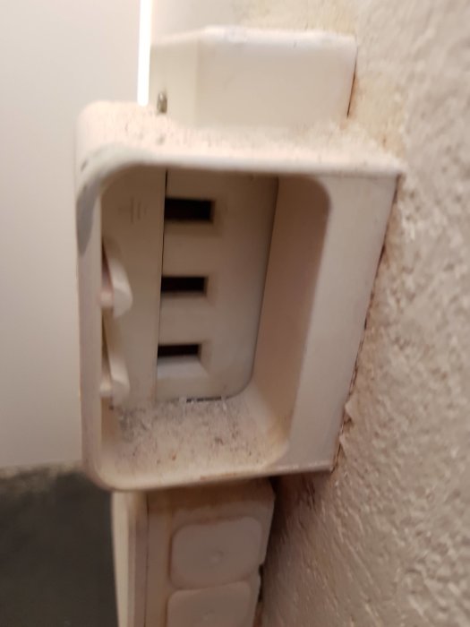 Öppet vägguttag med exponerade kontakter och damm, utan synlig sladd eller spis.