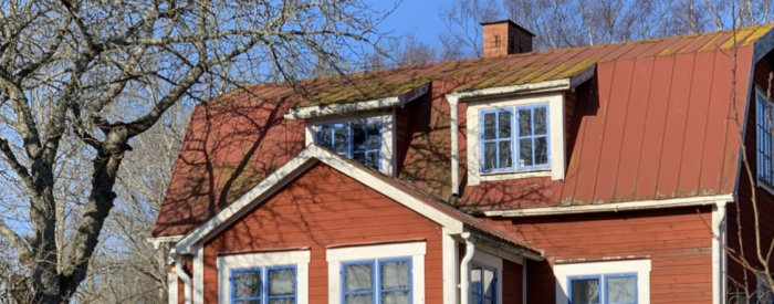 Detaljbild på rött hus med svängda takpannor och dörrfönster under klart himmel.