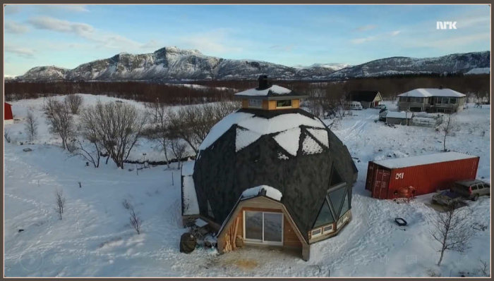 Geodesisk dom i snölandskap med berg i bakgrunden och en container bredvid.