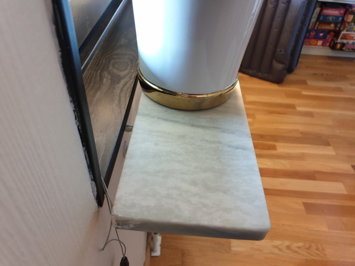 Marmorfönsterbräda monterad på konsol nära fönster, med en metallvas ovanpå och parkettgolv i bakgrunden.