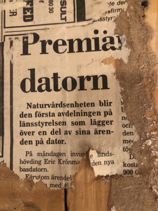 Nött och delvis riven tidningssida från mitten av 1980-talet med rubriken "Premiärdatorn" som hittats under renovering.