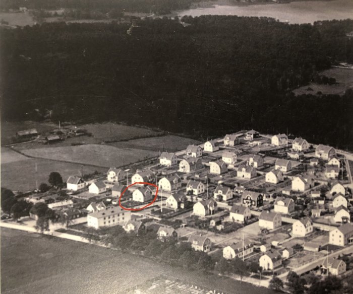 Svartvit flygbild från 1935 över egnahemsområde med markerat hus, omgivet av fält och skog.