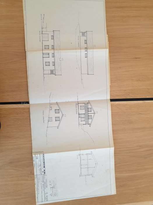 Arkitektritningar av ett hus med fasadvy och planlösning på ett bord.