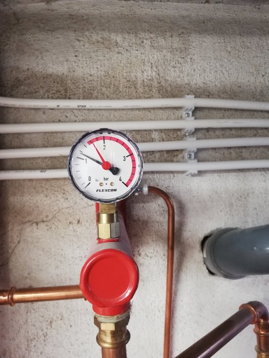 Manometer som visar 1 bar på en uppvärmningsanläggnings expansionskärl med vita rör i bakgrunden.