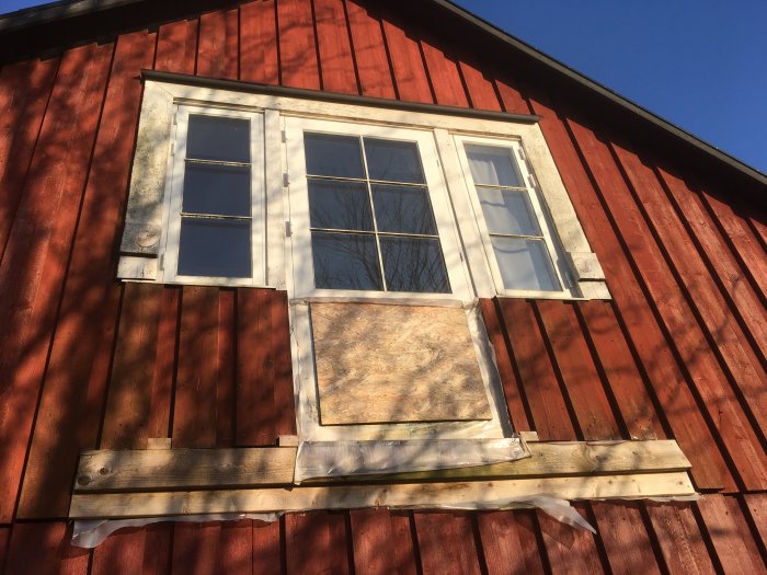 Renoveringsmaterial levererat till rödfärgad stuga med vita fönsterramar och oskyddad isolering.