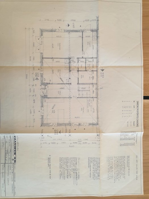 Arkitektonisk ritning av husplan med mått och noteringar på ett skrivbord.