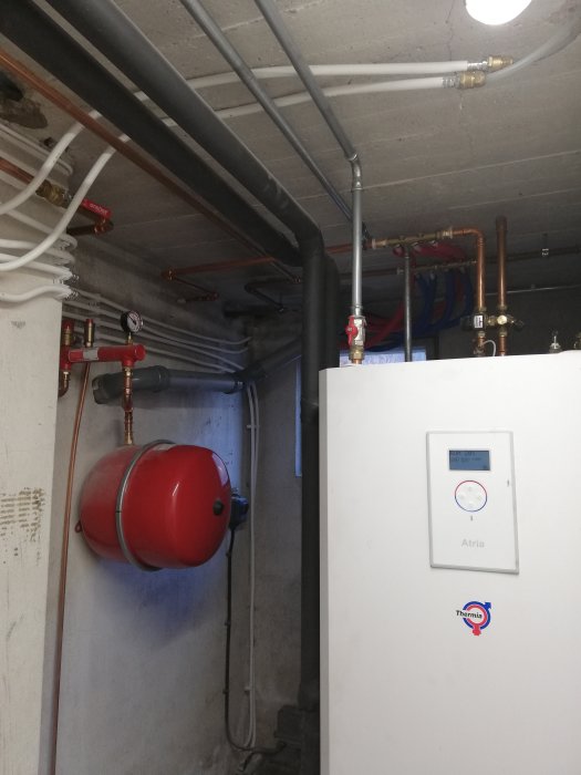 VVS-installation i källare med expansionskärl, rör och mätare på vägg.