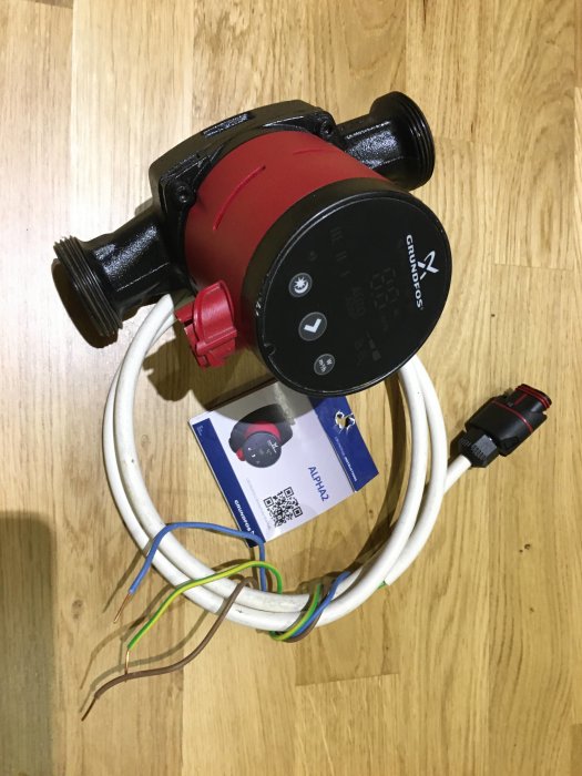 Använd Grundfos cirkulationspump modell 25-60 180 med anslutningskabel och manual på trägolv.