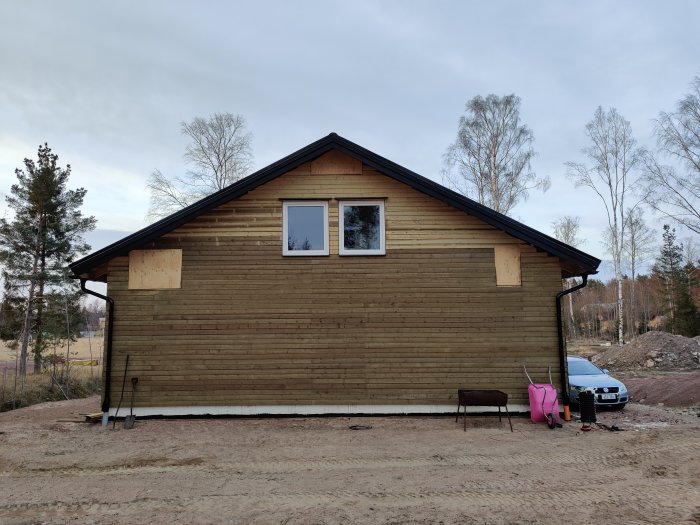 Hus under renovering med ny panel på sydfasaden, oavslutade sektioner och verktyg utanför.