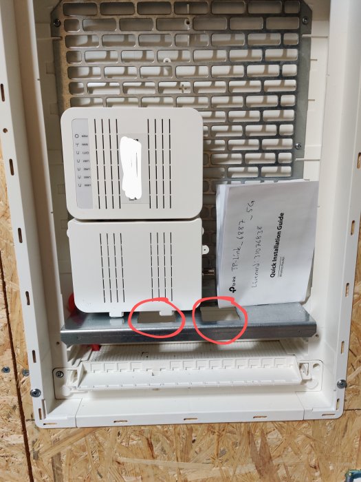 Nätverksskåp med fibermodem felplacerat för eluttag och installationsguide i bakgrunden på en OSB-panel.