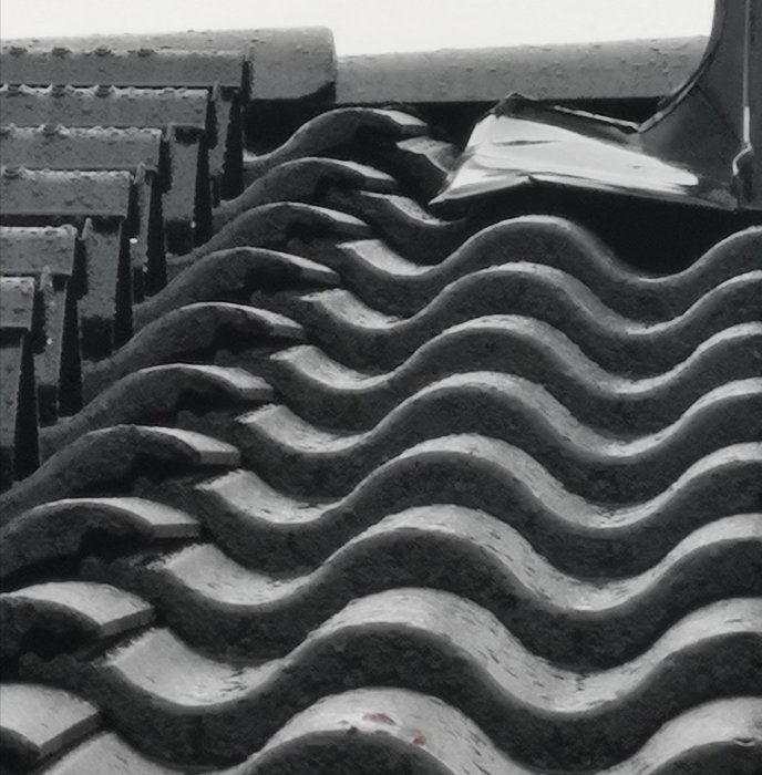 Närbild av ett svart tak med vågformade takpannor där vissa pannor är skadade och har glipor.