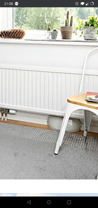 Vitmålat rum med radiator, rörledningar till element och ett fönster med krukväxter.