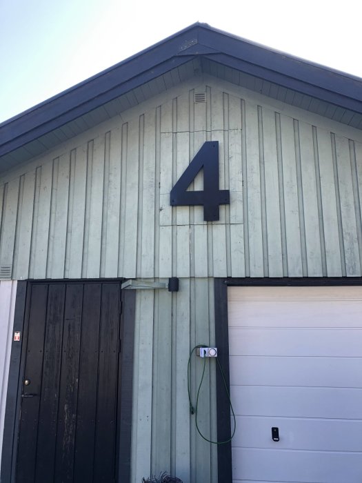 Stort nummer 4 monterat på en trävägg ovanför en garagedörr på ett hus.