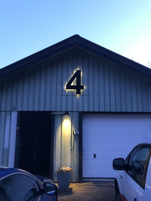 Husfasad i skymningen med nummer 4 upplyst ovanför garageport och en elbilsladdare.