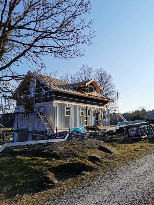 Hus under renovering utan ställning på framsidan med byggmaterial på marken en solig dag.