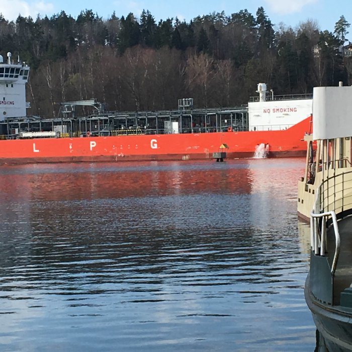 Röd LPG-tanker med texten 'NO SMOKING' som flyter förbi i en flod.