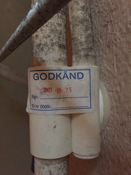 Etikett på ett rör med texten "GODKÄND 2003-09-25" och "ID nr 2000-", som visar på åldern och godkännandet av badkaret.