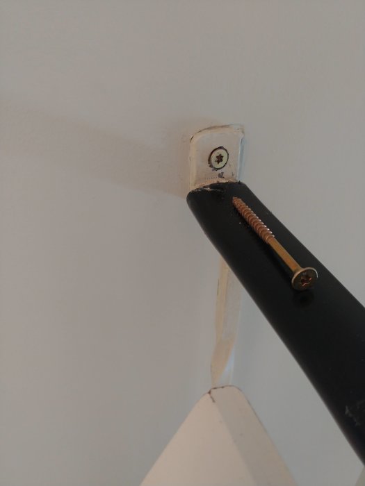 Et trapperrekkverk med skruer festet til veggen. En ny kraftig treskrue ligger langs et svart metallstykke, klar for montering i trekonstruksjonen.