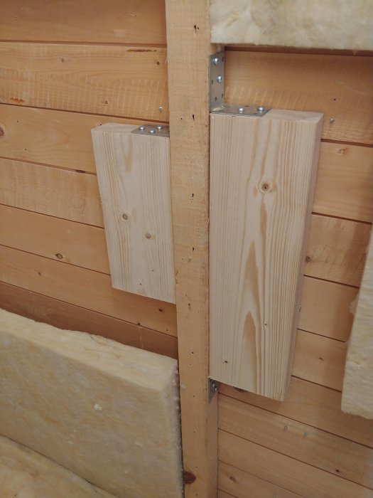 To vertikale trebjelker festet med metallbeslag på innvendig vegg.