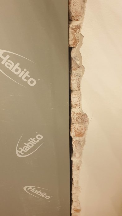Ojämn tegelvägg med stort mellanrum mot en ny gipsplatta på en byggarbetsplats.
