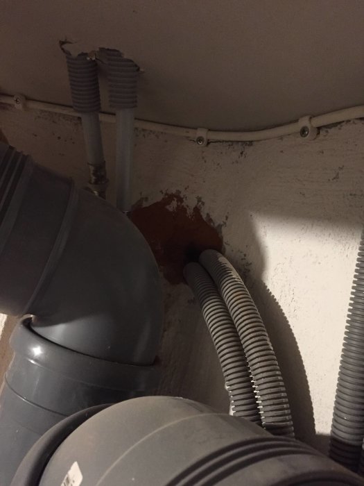 Källarhörn med vitmålade väggar och rött damm vid anslutning av rör, eventuell färgavflagning.