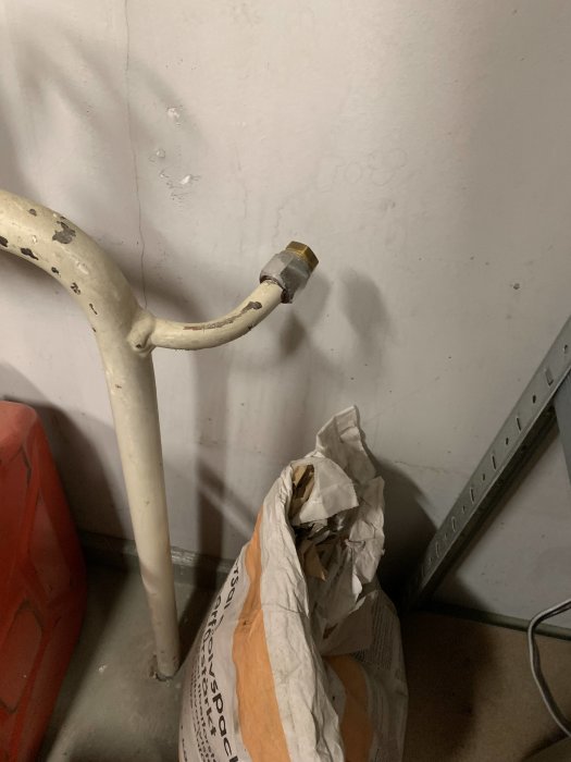 Kort rörstump med avkapad vattenkran nära en garagevägg, med ledningar och byggmaterial synliga i förgrunden.