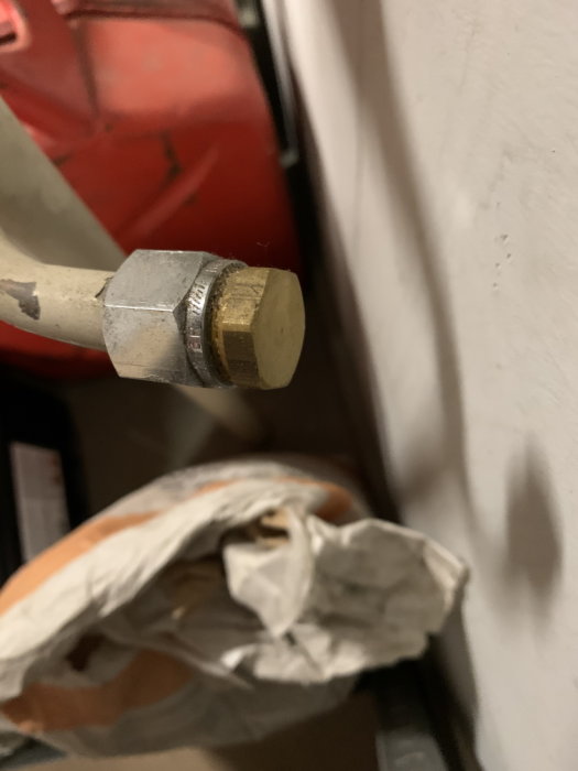 Avkapad vattenledningsstump nära en vit vägg i ett garage, med fokus på anslutningsdelen.