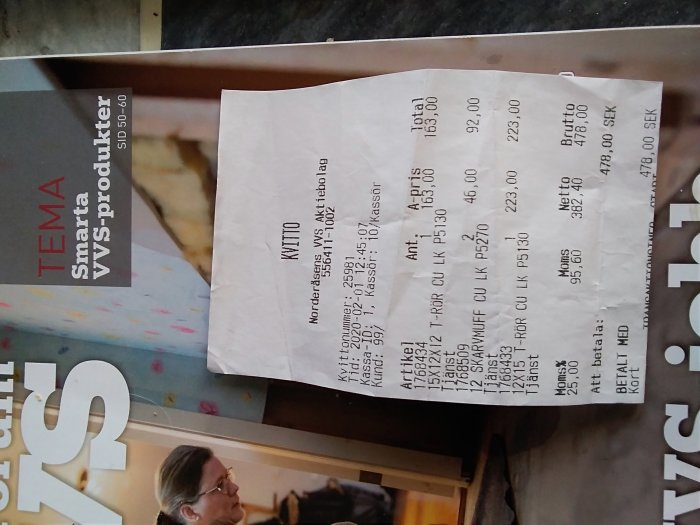 Kvittot från en Comfort butik med flera byggvaror listade och den totala summan, placerat ovanpå ett magasin.