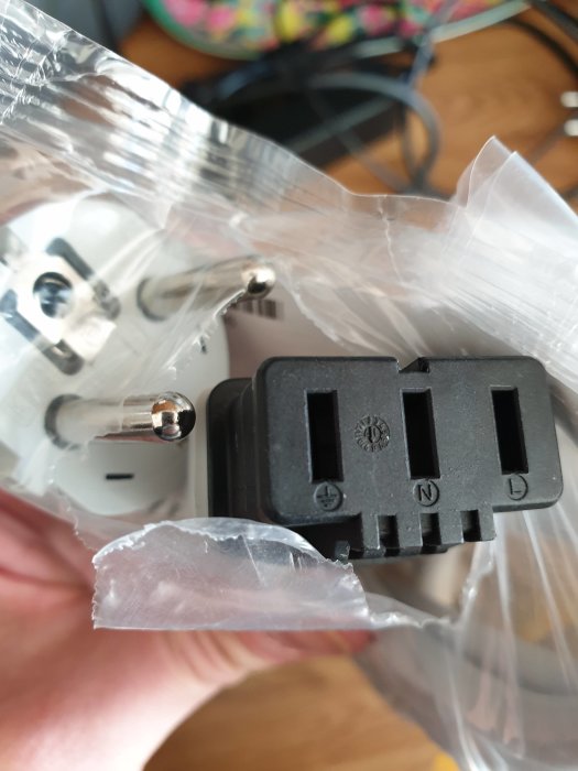 Hand håller en ny 230V ugnssladd med öppen ände, fortfarande i förpackningsplast.