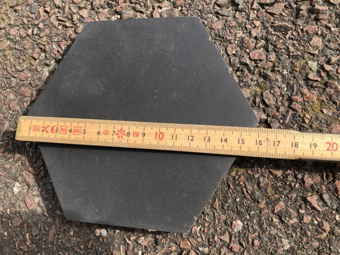 Svart klinkerplatta med måttstock visande tjocklek på 13 mm mot grusig mark.