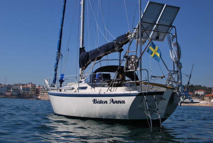 Segelbåt med namnet "Båten Anna" för ankar nära kusten under klarblå himmel.