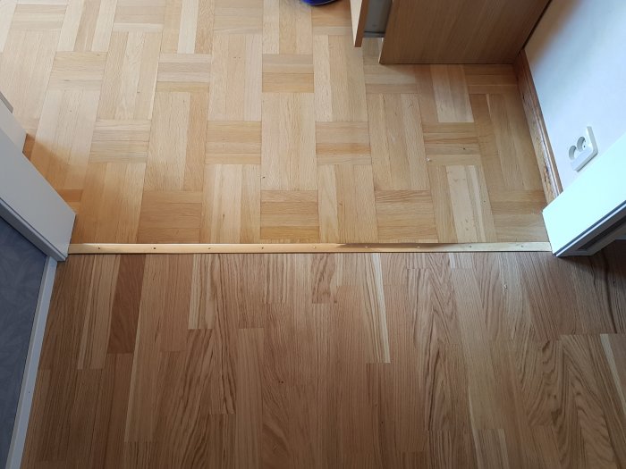 Två olika trägolv möts vid en tröskel, övre delen är parkett och nedre är laminat.